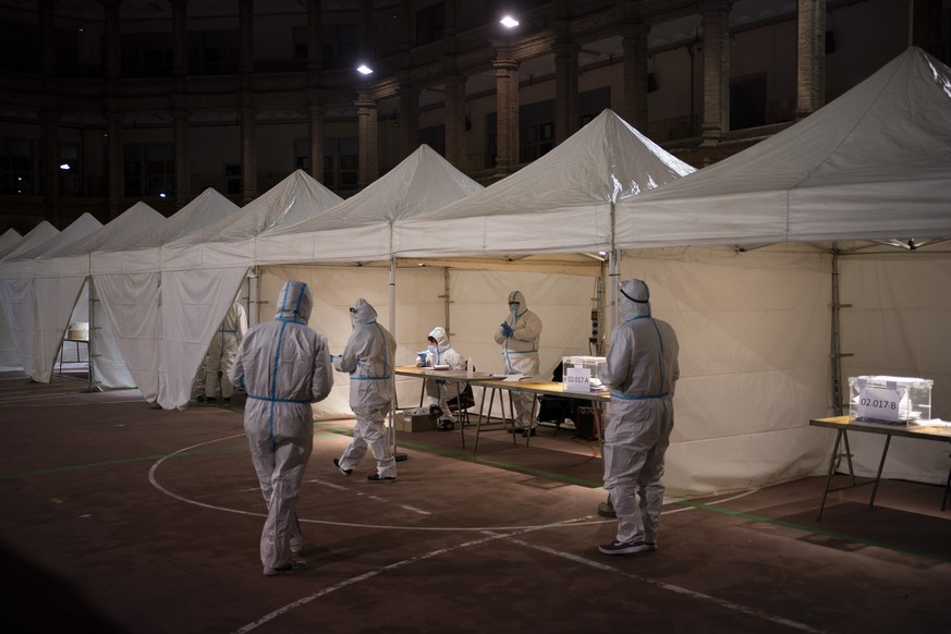 Electoral workers wearing protective suits as a precaution against coronavirus, wait for people to cast their vote at a polling station during the Catalan regional election in Barcelona, Spain, Sunday ...