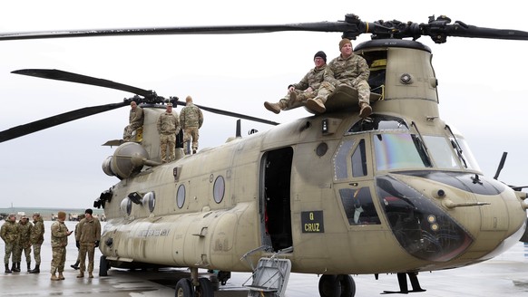 epa10552614 US servicemen rest on their Chinook transport helicopter, belonging to the US 101st Airborne Division, displayed for visitors on the runway after a ceremony of troop rotation of the Americ ...