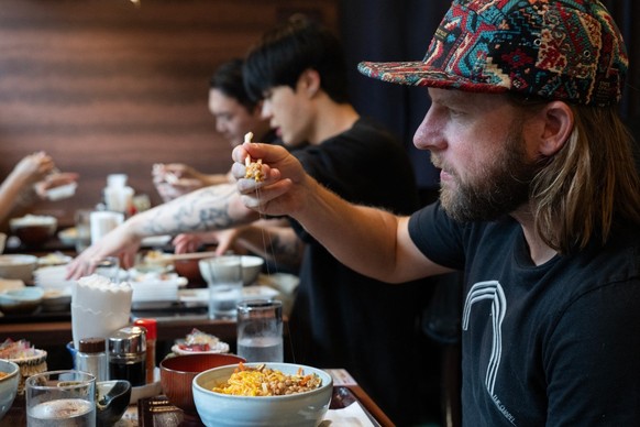 This photo taken on June 8, 2026 shows US tourist Wesley Smith looking at natto on his chopsticks as he eats lunch at the Natto Kobo Sendai-ya restaurant in Tokyo. The highly nutritious beans inoculat ...