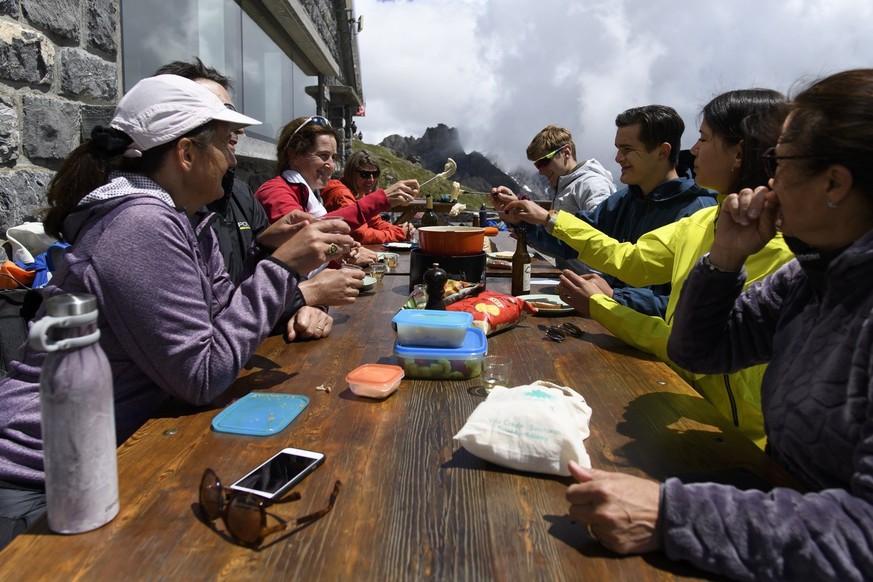 People eat a fondue on the terrace of the mountain hut Cabane Rambert, on Saturday, June 20, 2020, in the canton Valais, Switzerland. The cabin opens this weekend following the end of lockdown to figh ...