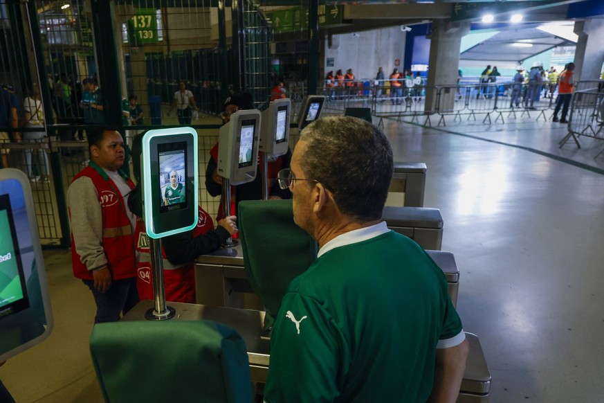 A man sits in front of a facial recognition machine at the entrance to the Allianz Parque stadium in Sao Paulo, Brazil on October 11, 2025. Facial recognition technology identifies and scans individua ...