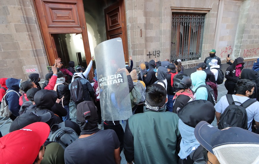 epa11202335 Hooded protesters vandalize one of the doors of the National Palace in Mexico City, Mexico, 06 March 2024. Mexicans protesting the disappearance of 43 Ayotzinapa students broke one of the  ...