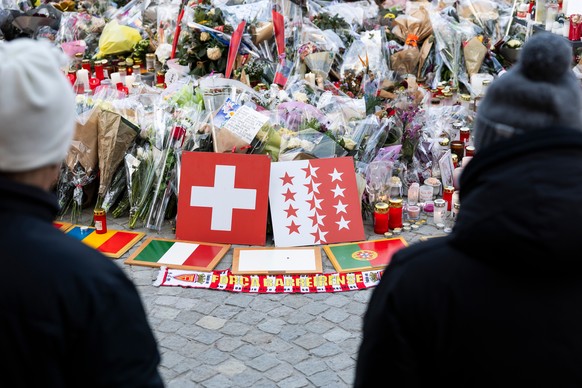 Plaques bearing flags representing Switzerland, Romania, Italy, Portugal, Belgium, France, and Turkey are placed along with flowers and candles to honor the victims of the fire at the "Le Constel ...