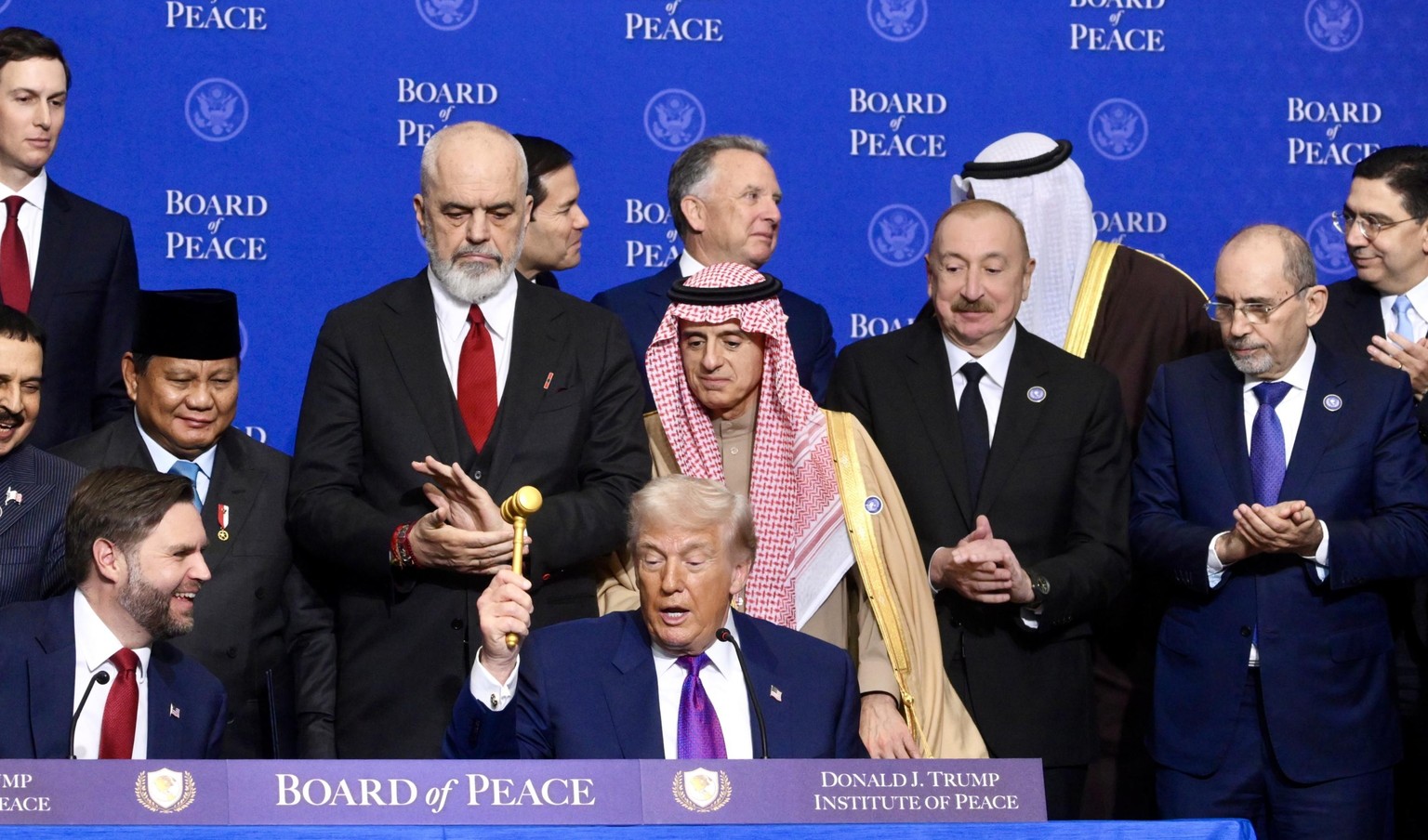 epa12759215 US President Donald Trump (C) raises the gavel during the Board of Peace meeting at the Donald J. Trump US Institute of Peace in Washington, USA, 19 February 2026. Established by Donald Tr ...