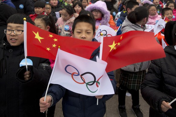 FILE - In this Feb. 27, 2018, file photo, a child waves a Chinese national flag and an Olympic flag during a ceremony to mark the arrival of the Olympic flag and start of the flag tour for the Winter  ...