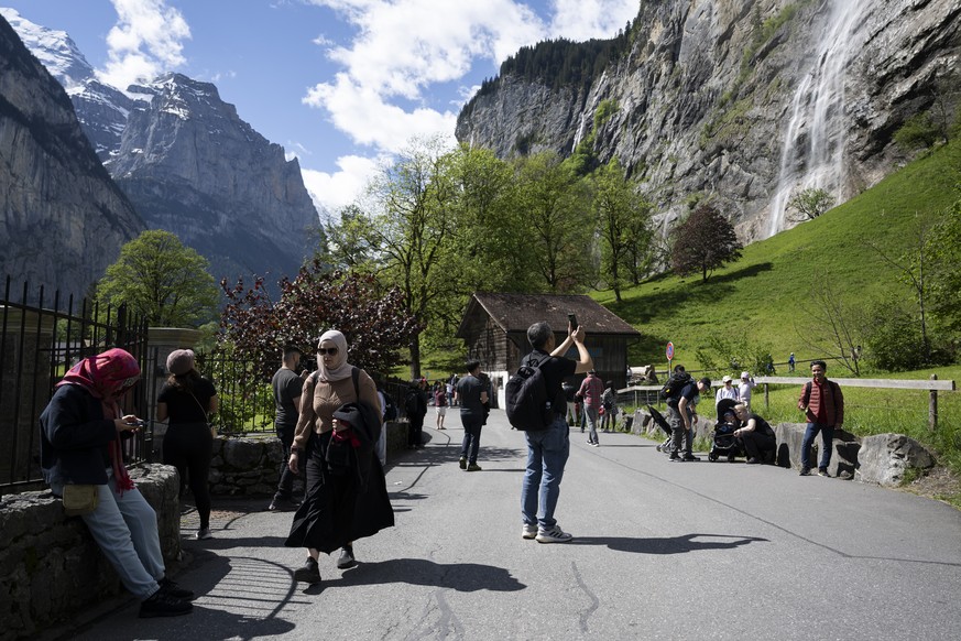 Touristen spazierendurch das Dorf Lauterbrunnen im Berner Oberland mit dem Staubbachfall im Hintergrund, am Sonntag, 19. Mai 2024. Der Ferienort Lauterbrunnen moechte eine Eintrittsgebuehr fuer Tagest ...