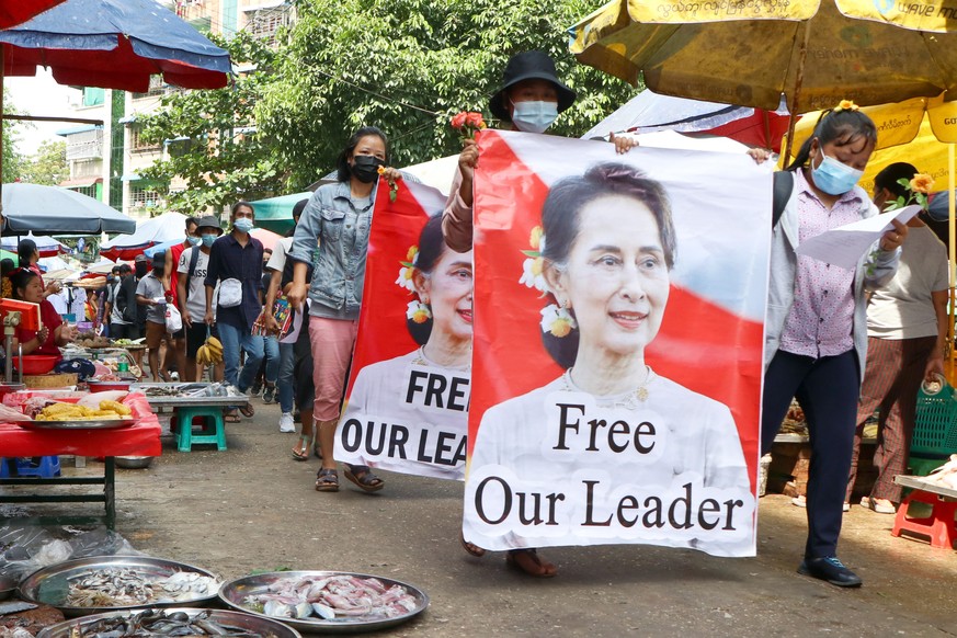 FILE - Protesters walk through a market with posters of ousted Myanmar leader Aung San Suu Kyi at Kamayut township in Yangon, Myanmar, on April 8, 2021. A Myanmar court convicted Suu Kyi in more corru ...