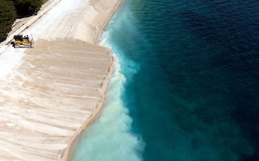 Cette vue aérienne montre un bulldozer en train de draguer des pierres pour restaurer les plages artificielles de Primosten, une ville côtière de Croatie