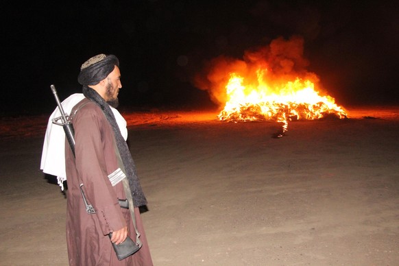 epa13123586 A Taliban official stands guard during drug burning in Kandahar, Afghanistan, 20 July 2026. Afghan authorities destroyed more than 13,000 kilograms of confiscated narcotics and 66,000 into ...