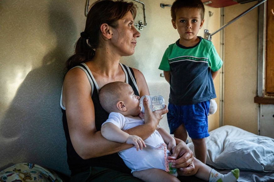 POKROVSK, DONETSK, UKRAINE - 2022/08/06: Mother Sanya (L) feeds her baby Yanosova (C), as they evacuate with her other child Sergei (R) and her mother Lumelia on the evacuation train to Dnipro. As fig ...