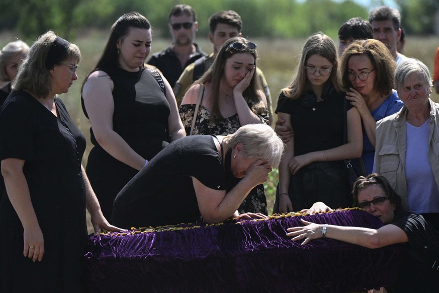 Des proches et des amis pleurent devant un cercueil lors des funérailles de Mykyta et Sofia Lamekhov et de leur fils Lev dans un cimetière de Sloviansk.