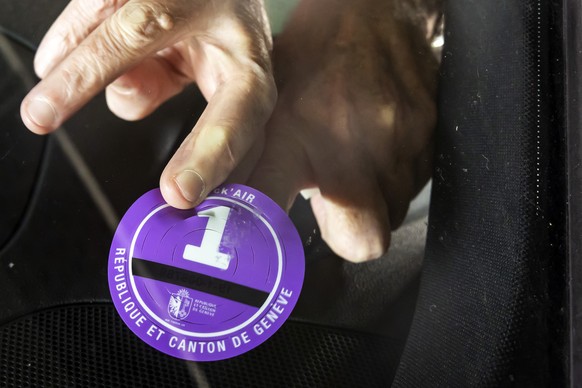 Une personne colle un Stick&#039;Air de categorie 1 sur le pare-brise de sa voiture, car le trafic motorise au centre ville est limite aux seuls vehicules munis d&#039;un macaron Stick&#039;Air de 0 a ...