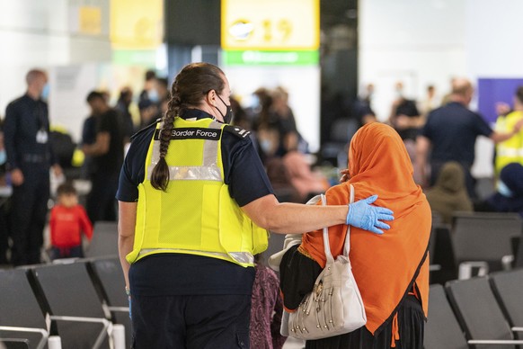 A member of Border Force staff assists a female evacuee from Afghanistan who arrived aboard an evacuation flight at Heathrow Airport in London, Thursday Aug. 26, 2021. The U.K. defense ministry has organised an air-lift of vulnerable citizens from Kabul, following the Taliban assuming power in Afghanistan. (Dominic Lipinski/Pool via AP)