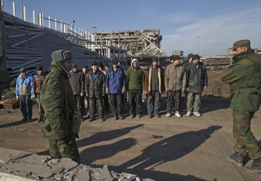 Ukrainian prisoners of war stand as Russia-backed separatists watch after removing bodies of Ukrainian servicemen from the rubble of the airport building, seen in the background, outside Donetsk, Ukra ...