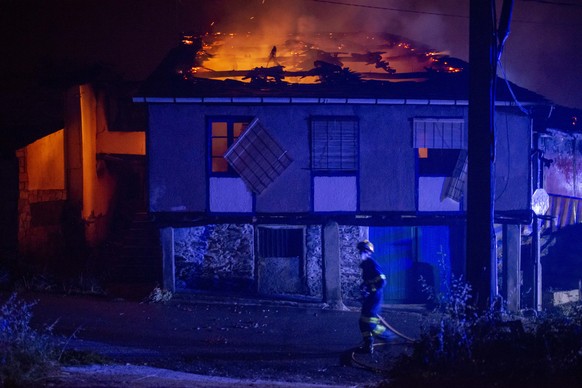 epa10077183 A firefighter walks past a house on fire in the village of Alixo, O Barco de Valdeorras, Galicia, northwestern Spain, 18 July 2022. The forest fire had destroyed some 2,400 hectares as of  ...