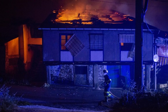 epa10077183 A firefighter walks past a house on fire in the village of Alixo, O Barco de Valdeorras, Galicia, northwestern Spain, 18 July 2022. The forest fire had destroyed some 2,400 hectares as of ...