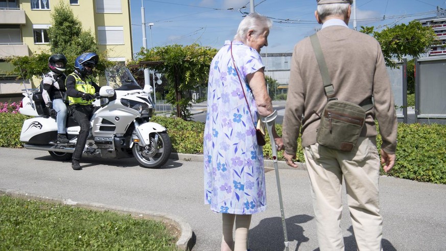 Un motard roule avec sa moto devant un couple de personnes âgées, quelque part en Suisse.