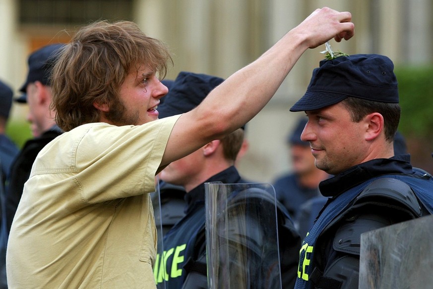 A protesters puts a flower on the cap of a riot police officer during a peaceful protest against the G8 summit in Lausanne, Switzerland, Saturday, May 31, 2003. The G8 summit will take place from June ...