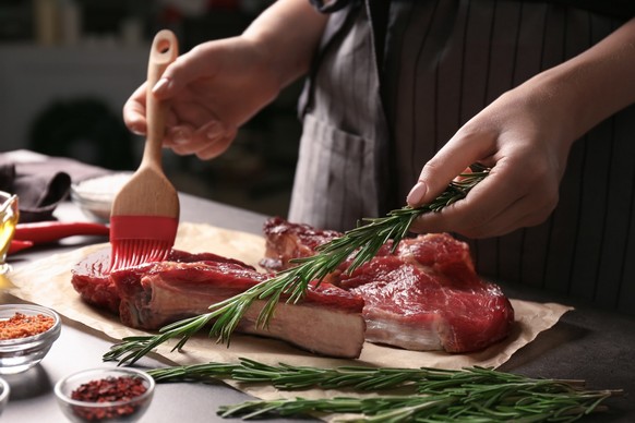 Woman applying oil onto raw steak with silicone brush in kitchen