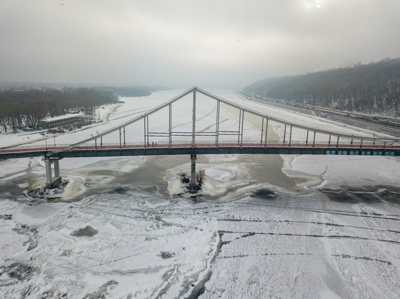 Aerial drone view. Pedestrian bridge over the frozen Dnieper River in Kiev. Cloudy frosty winter morning, frosty pattern on ice.