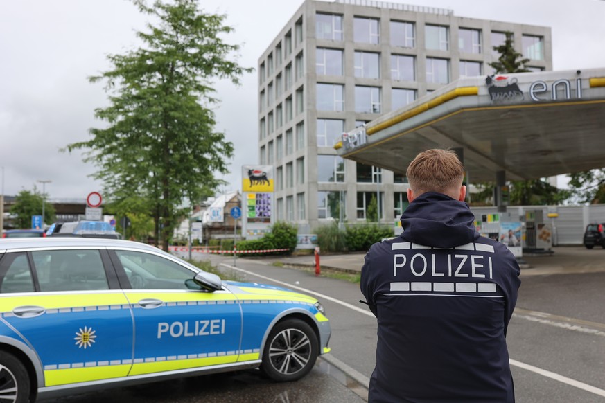 07.07.2024, Baden-Württemberg, Konstanz: Ein Bereich nahe einer Tankstelle ist mit Absperrband gesichert, davor ist ein Polizeiwagen und ein Polizist zu sehen. Nach mehreren Schüssen auf eine Menschen ...