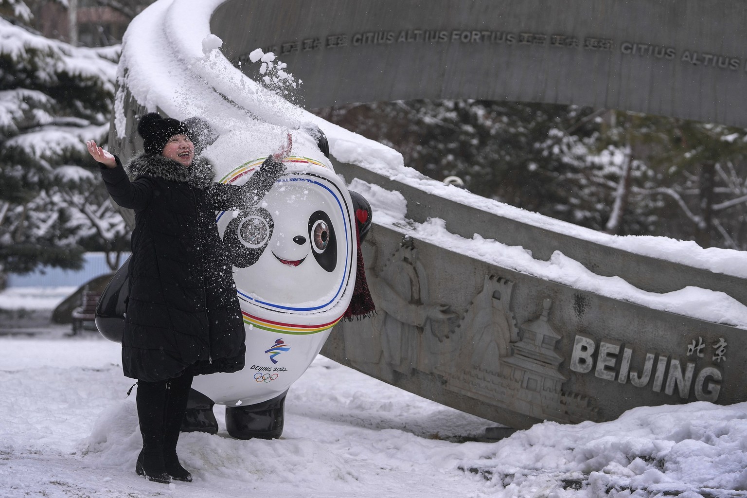 A woman throws snow near the Bing Dwen Dwen, the Beijing Winter Olympics mascot, on display at an Olympics monument during a snow fall in Beijing, Sunday, Feb. 13, 2022. (AP Photo/Andy Wong)