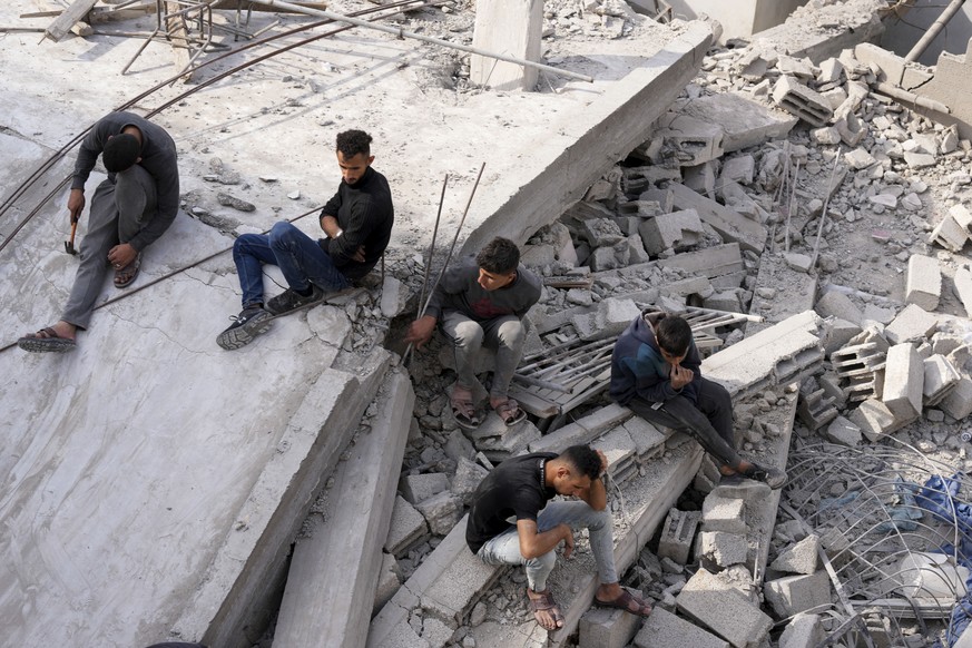 Palestinians sit by the building of the Al-Nadi family destroyed in the Israeli bombardment of the Gaza Strip in Nusseirat refugee camp, central Gaza Strip, early Friday, Dec. 8, 2023. (AP Photo/Adel  ...