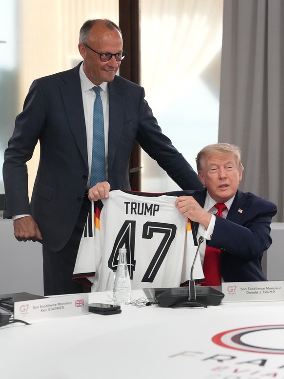 U.S. President Donald Trump, right, holds up a jersey with the number 47 on it presented to him by German Chancellor Friedrich Merz, left, during a working session at the G7 summit in Evian-les-Bains, ...