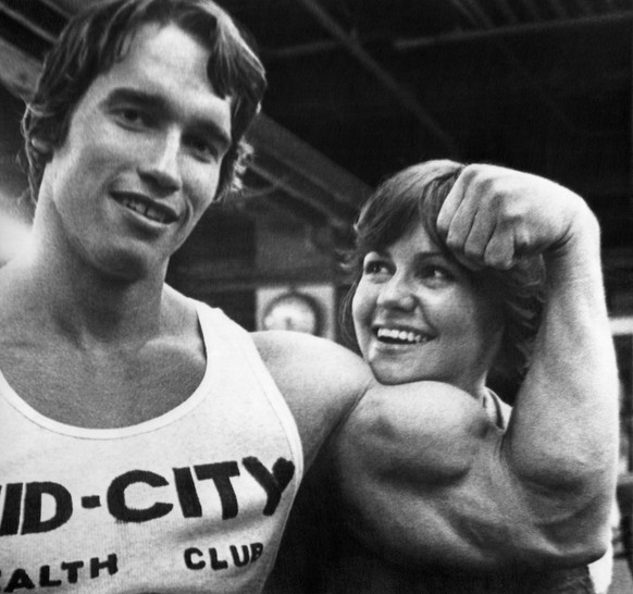 Mister Universe Arnold Schwarzenegger of Austria supplies chinrest for Sally Field, The Flying Nun, as they take a break from a body-building workout session in New York, April 20, 1976. They began th ...