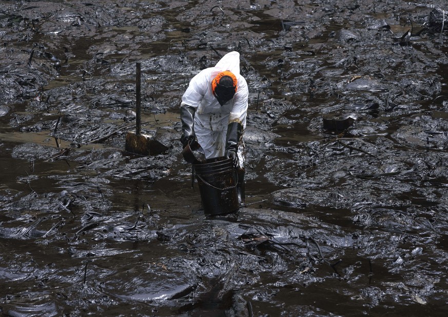 A worker cleans oil from Cavero Beach in the Ventanilla district of Callao, Peru, Friday, Jan. 21, 2022. The oil spill on the Peruvian coast was caused by the waves from an eruption of an undersea vol ...