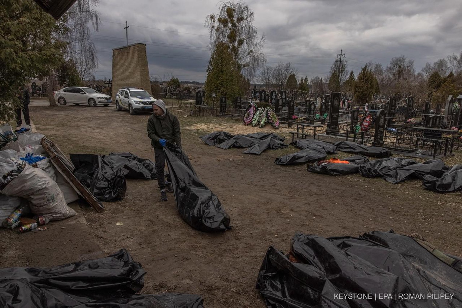 epa09874650 A man pulls a body bag with a killed person who was brought to the cemetery during the identification process by police officers and forensic personnel, in Bucha, northwest of Kyiv, Ukrain ...