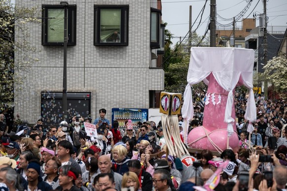 Tourists look on and take photos as devotees carry a large phallus-shaped portable shrine through the streets of Kawasaki during the Kanamara festival on April 5, 2026. Showcasing phallus-shaped porta ...