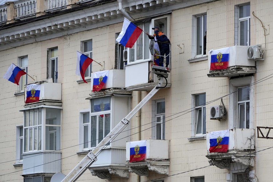 Workers hang Russian flags at an apartment building in Luhansk, Luhansk People's Republic controlled by Russia-backed separatists, eastern Ukraine, Tuesday, Sept. 27, 2022. Voting began Friday in ...