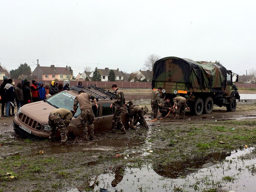 Des soldats essayent tant bien que mal d'extraire leur véhicule de la boue, sous le regard des migrants.