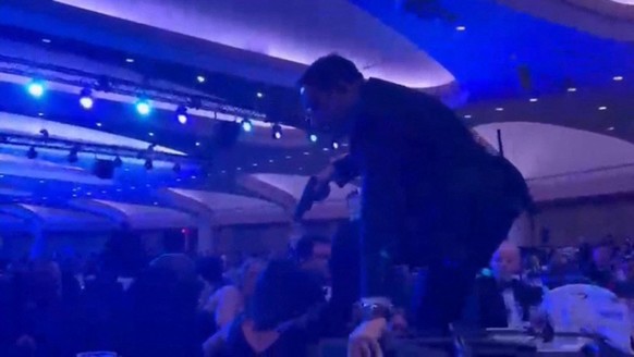 A screen grab taken from a video filmed by an AFP reporter shows an armed agent climbing over chairs as they move to the stage after loud bangs were heard during the White House Correspondents' d ...