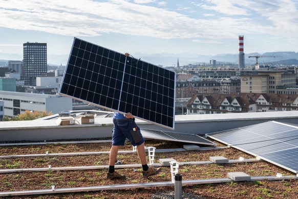 Un technicien d’une entreprise d’installation électrique monte une installation solaire sur le toit d’un immeuble d’habitation à Zurich.