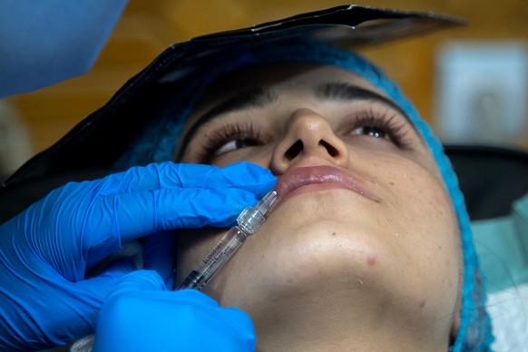In this photograph taken on August 13, 2025, a member of the medical staff injects fillers into an Afghan women&#039;s lips at a beauty clinic in Kabul. Decked with fake crystal chandeliers and velvet ...