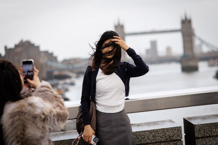 epa11738472 A woman poses for a photo on the London Bridge on a windy day in London, Britain, 24 November 2024. National severe weather warnings are still in place across the UK as Storm Bert already  ...