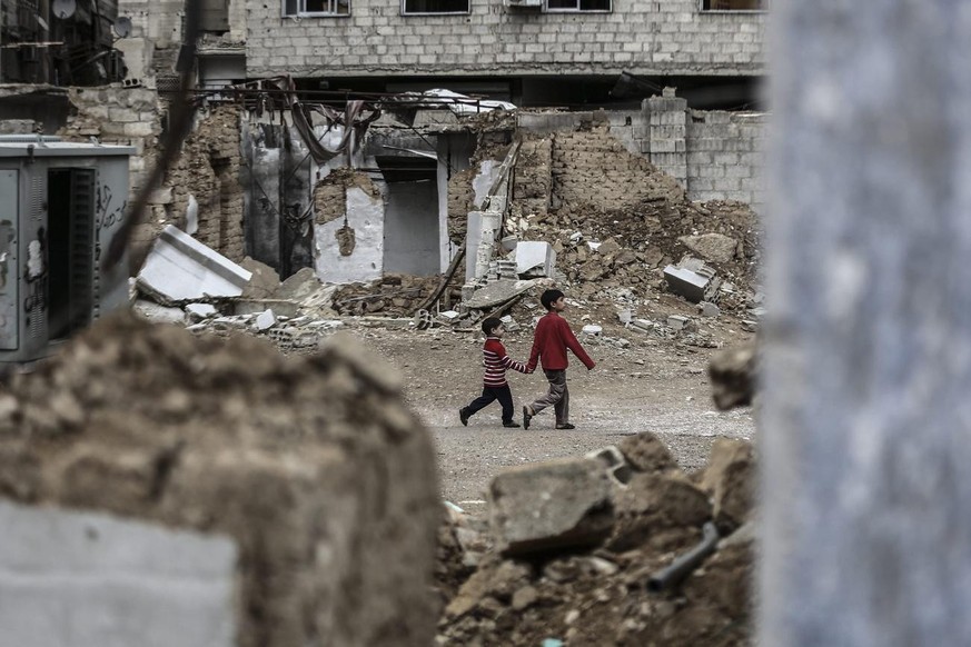 epa04995259 Two young Syrian boys hold hands as they walk past destroyed houses in rebel-held area of Douma, outskirts of Damascus, Syria, 25 October 2015. More than 250,000 people have died in the Sy ...