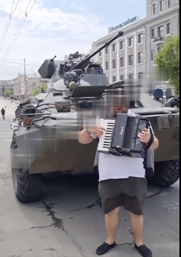 Un musicien de rue, jouant pour les mercenaires Wagner, devant l'un de leurs tanks.