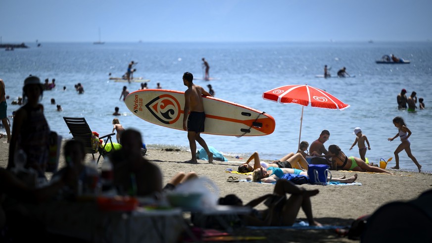 People cooling off in the shade of trees and a person carries his paddle board during warm weather on the shore of the Lake Geneva at the Vidy beach (plage de Vidy) in Lausanne, Switzerland, Sunday, J ...