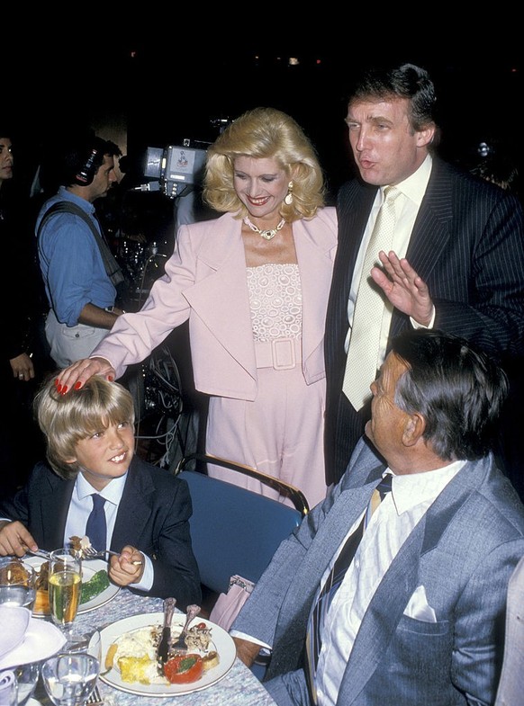 View of, from left, Donald Trump Jr (seated), his parents Ivana Trump (1949 - 2022) &amp; Donald Trump (standing), and Milos Zelnicek (1927 - 1990) (Ivana&#039;s father), as they attend a boxing match ...