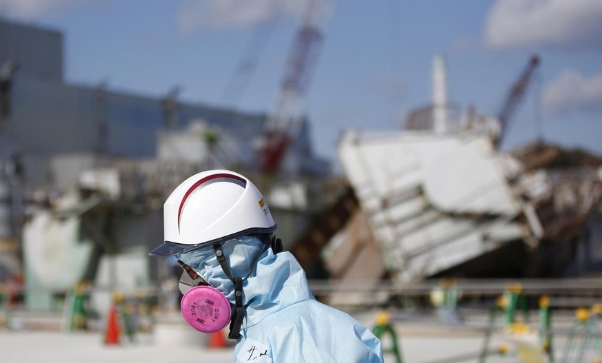 A Tokyo Electric Power Co. (TEPCO) employee, wearing a protective suit and a mask, walks in front of the No. 1 reactor building at the tsunami-crippled Fukushima Dai-ichi nuclear power plant in Okuma, ...