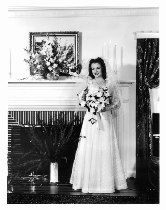 Marilyn Monroe, on the day of her wedding day to James Dougherty, in front of a fireplace in her wedding dress and holding a bouquet, Los Angeles, 1942. (Photo by Getty Images)