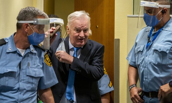 (FILES) Ex-Bosnian Serb military chief Ratko Mladic removes his facemask as he arrives in the courtroom prior to the hearing of the final verdict on appeal against his genocide conviction over the 199 ...