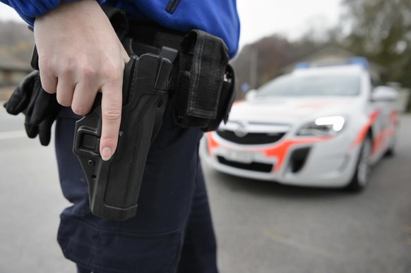 [Editor&#039;s note: photo mise-en-scene] A policer officer of the cantonal police of Vaud has takes hold of gun, in the foreground, while a police car is seen in the background, photographed in Cugy, ...