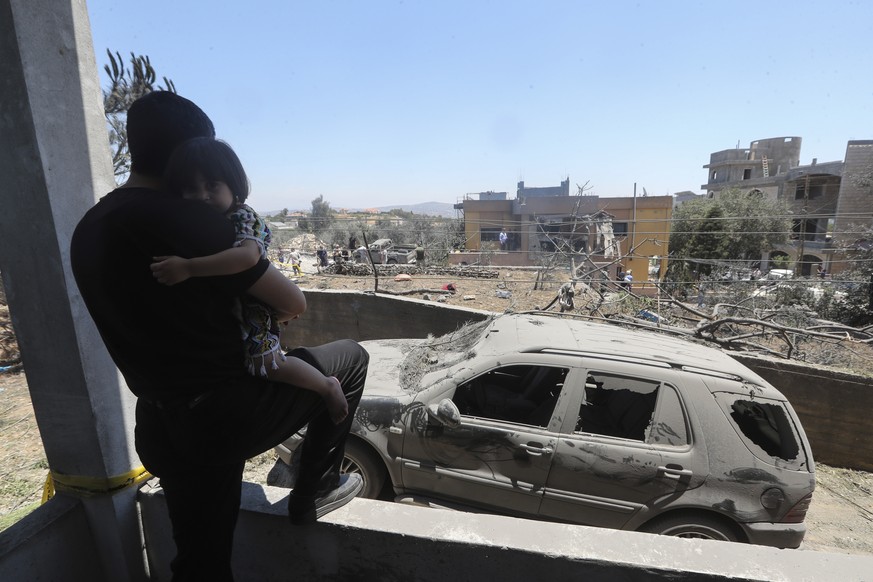 A man holds his child as he looks at the damage that was caused by an Israeli airstrike late Thursday, in the southern village of Jmaijmeh, Lebanon, Friday, July 19, 2024. Lebanon&#039;s militant Hezb ...
