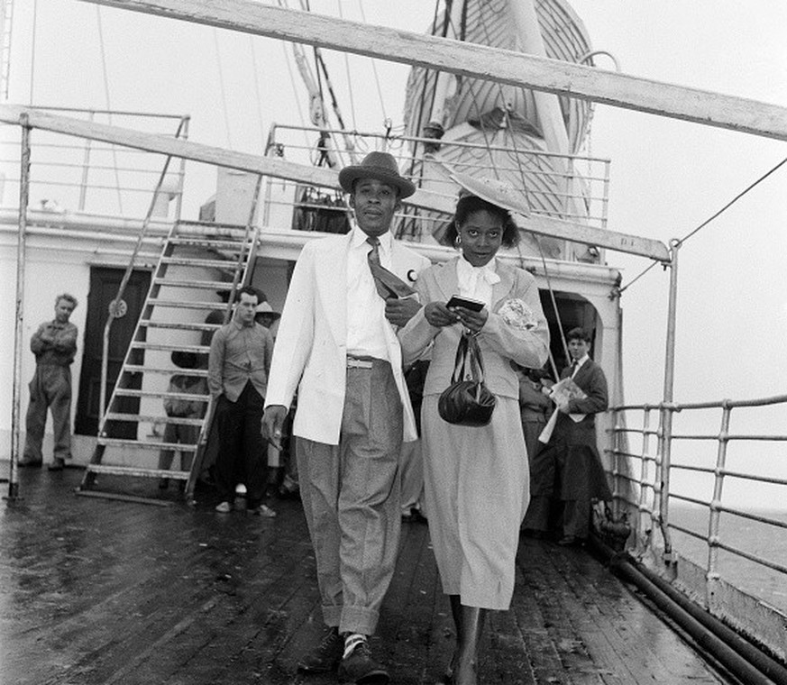 Louise Robinson, a 19 year old Jamaican dressmaker, in a grey costume and pale blue hat, has a last minute stroll on deck before going to the immigration authority at Plymouth. With her is Nathaniel D ...