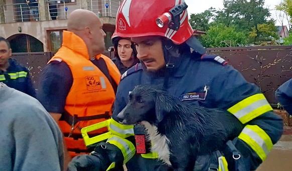 epa11603979 A handout photo made available by the Romanian General Inspectorate for Emergency Situations (IGSU) shows a Romanian rescuer carrying a dog in his arms, in the flood-affected village of Pe ...