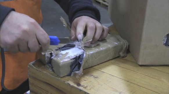 In this image released by the Dutch Interior and Justice Ministry on Friday Oct. 12, 2012, showing a customs officer as he cuts into a block of cocaine, displayed Thursday Oct. 11, 2012. More than eig ...